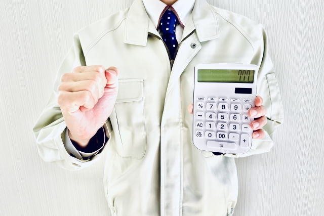 電卓を持ち指を指す作業服の人物